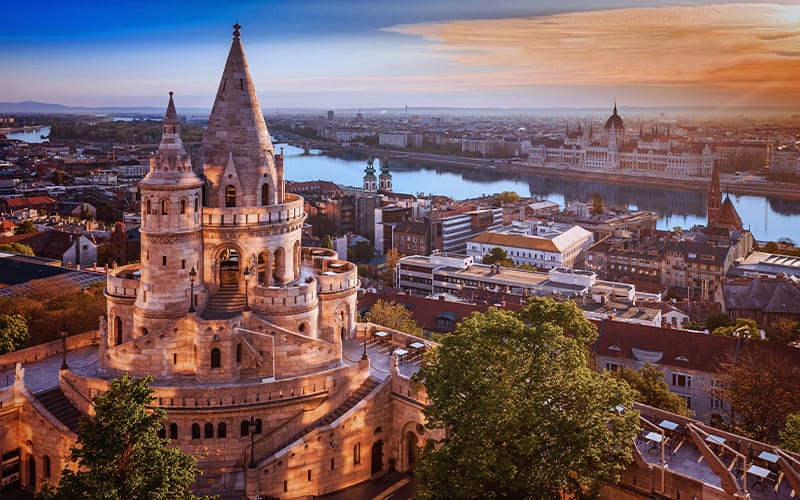 Vista panorámica desde el Bastión de los Pescadores hacia el río Danubio y el Parlamento de Budapest al atardecer.