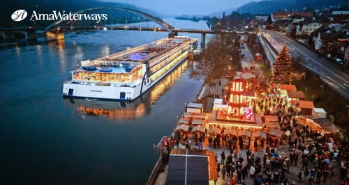 Barco de crucero fluvial de AmaWaterways iluminado junto a un mercadillo de Adviento en el río Rin.