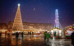 Plaza iluminada con un gran árbol de Navidad y una rueda de la fortuna durante la temporada de Adviento.