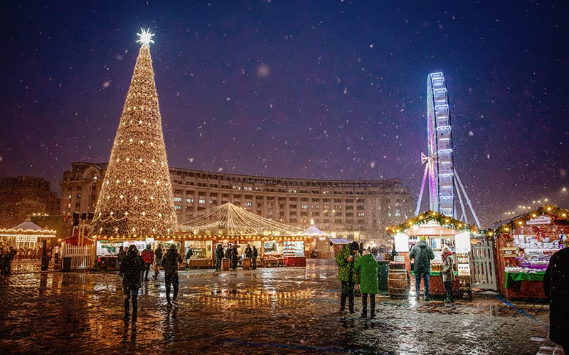 Plaza iluminada con un gran árbol de Navidad y una rueda de la fortuna durante la temporada de Adviento.